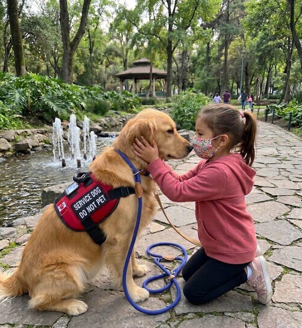 Isabella kneeling to touch noses with Biscocho, a golden retriever, in a park